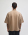 A unisex oversized boxy top in a light brown colour, featuring a minimal design and a branding logo.