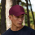 A burgundy six-panel heavy cotton cap on a model, set against a natural outdoor backdrop.