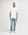 A model wears a white midweight T-shirt paired with black jeans and sneakers, featuring a logo on the shirt.