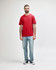 A red Gildan Softstyle adult midweight T-shirt displayed on a model wearing black jeans and shoes. The shirt has a logo.