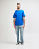 A man wearing a blue Gildan Softstyle adult midweight T-shirt paired with light denim jeans and white shoes.