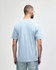 A person wearing a blue Gildan Softstyle adult midweight T-shirt, viewed from the back. The shirt has a logo.