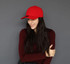 A red cotton/spandex cap is worn by a woman with long dark hair, smiling against a grey background.