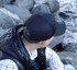 A black cotton/mesh cap worn by a person seated near rocks, with a reflective body warmer visible.