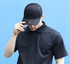 A black cotton and mesh cap with a logo, worn by a man in a black polo shirt against a blue background.
