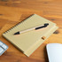 A tan notebook with a spiral binding and a black pen resting on top, placed on a wooden desk.