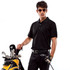 A man wearing a black polo shirt stands beside a golf bag, holding a club, with sunglasses on.