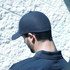 A dark grey cap featuring a textured waffle fabric design, viewed from the back against a stone wall backdrop.