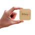 A hand holding a square bamboo wireless charger with the name "Riley" engraved on it.