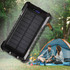 A black solar power bank with multiple charging ports, set against a camping scene with a tent and two people.