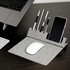 A grey foldable mouse pad with a phone holder and slots for pens, placed beside a laptop and keyboard.