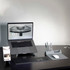 A sleek grey Ascend Mini Stand holding a smartphone, positioned beside a laptop, keyboard, and pen holder on a desk.