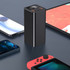A black power bank stands upright, surrounded by smartphones and a gaming console on a dark surface.