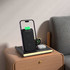 A magnetic wireless charger in black, positioned next to a phone on a wooden bedside table, with a small notebook and earbuds.