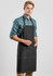 A man wearing a black denim apron with pockets, standing against a light grey background. The apron has a logo.
