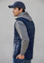A navy men's alpine vest with grey hooded sleeves, featured on a model facing sideways. The vest has a logo.