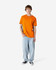 A heavyweight unisex t-shirt in bright orange, paired with light blue baggy jeans, modeled by a young person.