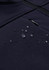 A dark navy softshell jacket with water droplets beading on the fabric, featuring a zippered pocket.