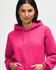 A bright pink hooded sweatshirt featuring a front pocket and drawstrings, worn by a model adjusting the hood.
