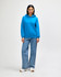 A woman in a bright blue hooded sweatshirt and jeans stands with her hands in the pockets.