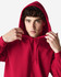 A red hooded sweatshirt is worn by a young man adjusting the hood near his face. The sweatshirt features a logo.