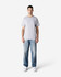 A man stands wearing a light grey Gildan Ultra Cotton Adult T-Shirt and blue jeans, with white sneakers.
