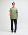 A model wearing a green unisex short sleeve T-shirt and black cargo pants, standing in a neutral setting.