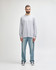 A grey long sleeve T-shirt worn by a man standing against a plain background, paired with light blue jeans.