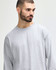 A grey long sleeve T-shirt on a model, featuring a relaxed fit and a simple design, with a branding logo visible.