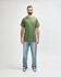 A green Gildan Heavy Cotton Adult T-Shirt, worn by a model paired with black jeans and sneakers, standing against a white background.