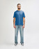 A model wearing a blue Gildan Softstyle adult T-shirt and light blue jeans, standing against a plain background.