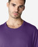 A man is wearing a purple Gildan Softstyle adult t-shirt, displaying a relaxed neckline and a casual style.