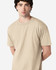 A midweight adult T-shirt in a neutral beige colour, displayed on a model with a casual pose. The shirt features a logo.