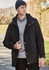 A model wearing a black jacket and a navy beanie, standing outdoors with greenery in the background.