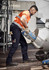 A man in orange and grey high-visibility workwear pours from a bag into a mixer, wearing navy rugged cargo pants.