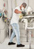 A man wearing light blue stretch jeans and a white t-shirt is spray painting in a workshop.