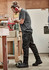 Men's rugged cooling stretch pants in black, featuring cargo pockets, are worn by a person working in a workshop.