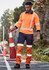 Hi-vis orange and navy work pants with reflective tape, worn by a man holding a traffic cone on a rural road.
