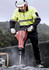 A worker in a fluorescent yellow and black hooped pullover operates a demolition tool at a construction site.
