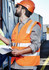 A man wearing an orange hi-vis zip vest with reflective stripes and a hard hat, holding documents at a construction site.