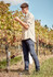 A light beige long sleeve button-up shirt is worn by a man in a vineyard, paired with navy pants.