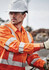 Hi-vis orange long sleeve work shirt with reflective tape, worn by a male worker in a construction setting, wearing safety gear.