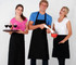 A group of three people wearing black short waist aprons, with one holding a tray of drinks and others preparing food.