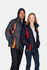 A sportech nylon jacket in navy and red, worn by a woman, alongside a man in a grey and orange jacket. Both feature logos.