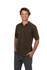 A man wearing a dark olive green cotton polo shirt, standing with hands in pockets and smiling. The shirt has a logo.