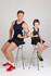 A man and a boy pose on stools, wearing black and blue singlets, showcasing a sporty style. The man has red shoes and the boy wears green shoes.