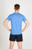 A blue heather T-shirt worn by a person from the back, paired with black shorts. The shirt features a logo.