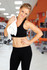 A smiling woman in a black athletic outfit holds a white towel, set in a gym environment with fitness equipment in the background.