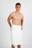 A white bath towel wrapped around a young man, standing upright and smiling against a plain background.