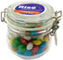 A glass canister filled with colourful chewy fruit candies, featuring a metal clasp and a logo on the lid.